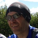 A picture of Jonathan France from the neck up. He is wearing a blue top, a headband and sunglasses